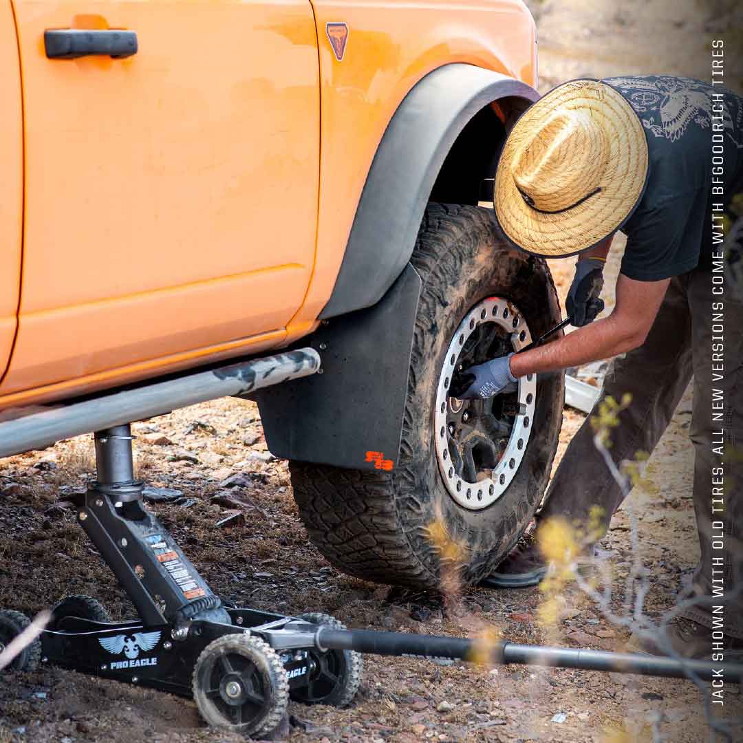 Off-road vehicle raised by a 2 Ton Big Wheel Jack, with a person working on the tire in a dusty setting.