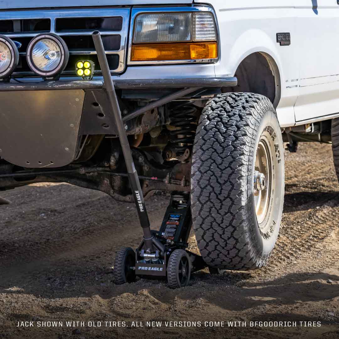 Off-road jack positioned under a lifted SUV with large tires and LED lights on the grill.
