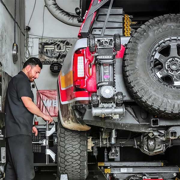 Mechanic working on a lifted red SUV with a mounted Pro Eagle winch and spare tire in a garage.