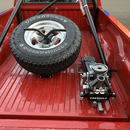 2 Ton off-road jack and spare tire in the bed of a red pickup truck.