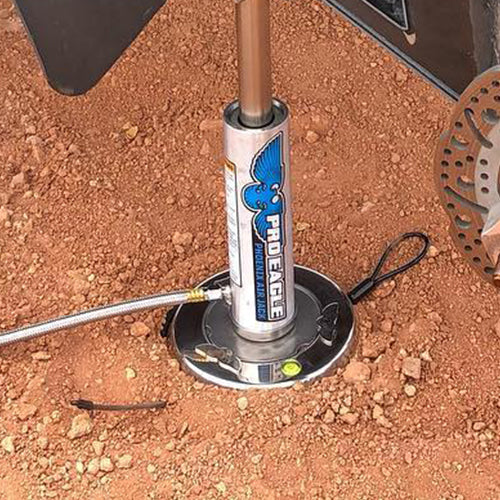 8-inch sand base for Phoenix Co2 Air Jack placed on red dirt, near a vehicle wheel.