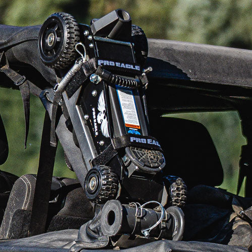 Black anti-rattle strap secures a Pro Eagle jack to a vehicle in a rugged outdoor setting.