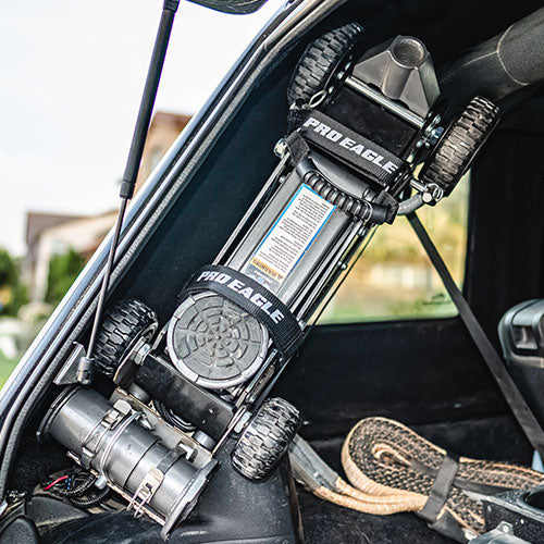 Anti-rattle strap on a Pro Eagle off-road jack mounted in a vehicle's trunk.