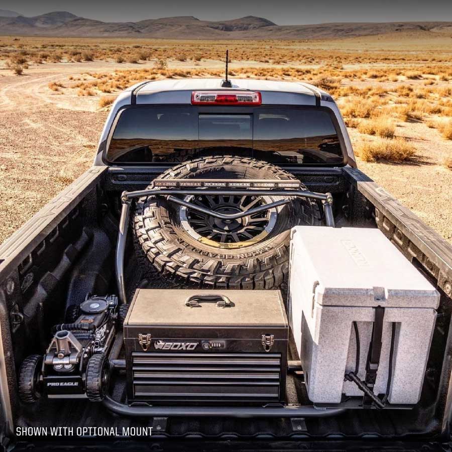 Truck bed filled with off-road gear including a large tire, a rugged jack, and storage boxes in a desert setting.
