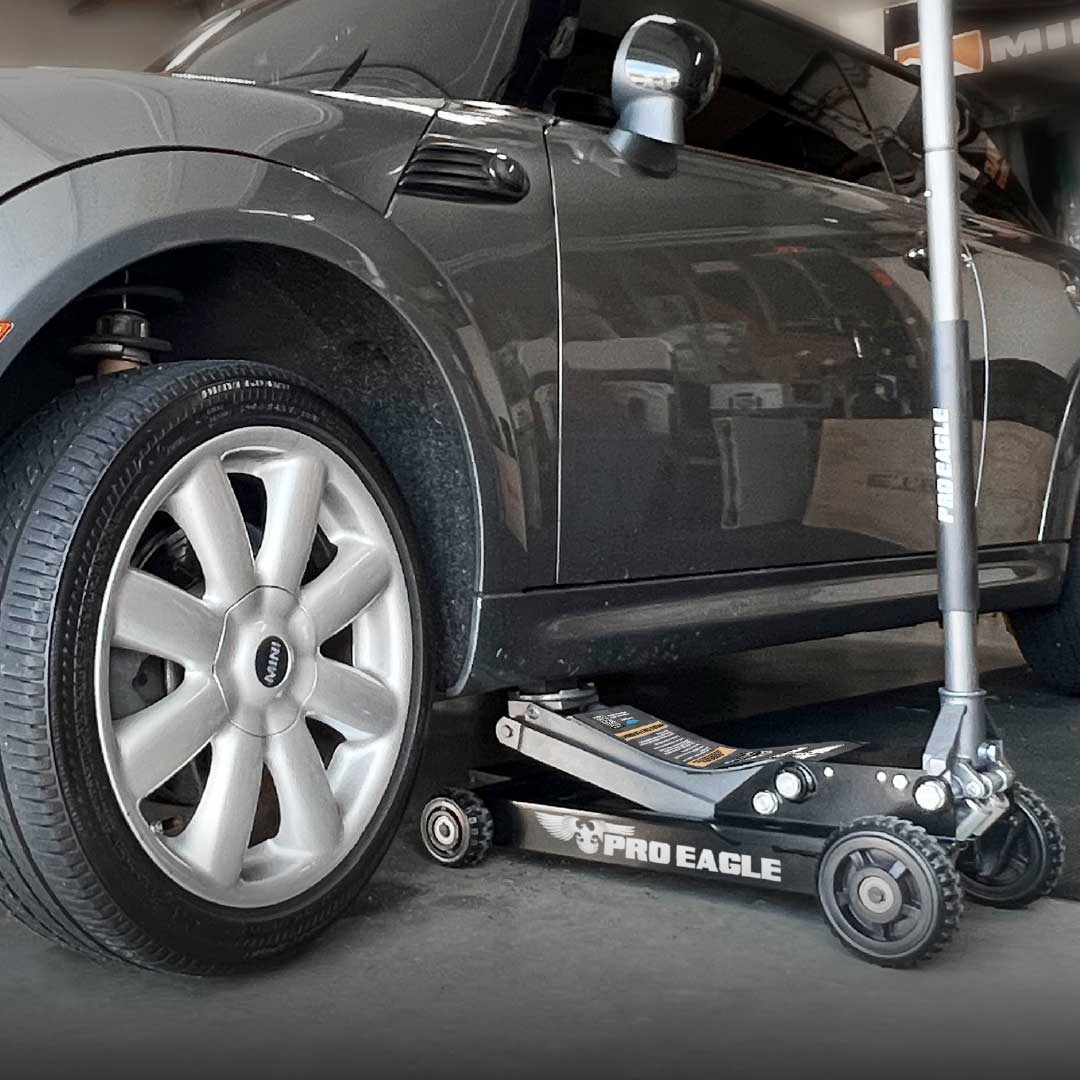 3 Ton Off Road Shop Jack "Abrams" positioned under a black car's wheel in a garage.