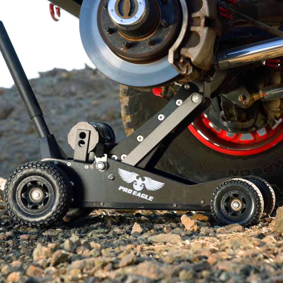 Black off-road vehicle jack, branded "Pro Eagle," with robust wheels on rocky ground, near a vehicle brake system.